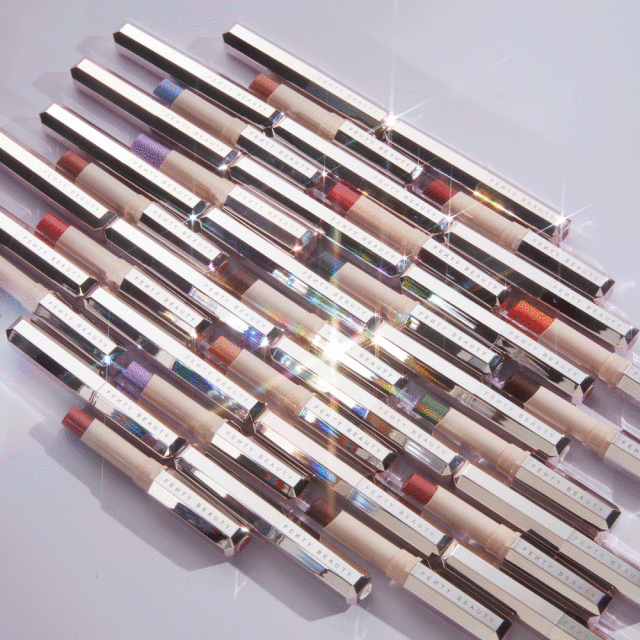 Arrangement of Fenty Beauty makeup sticks in varying shades on a white surface with studio lighting, highlighting product textures and colors.