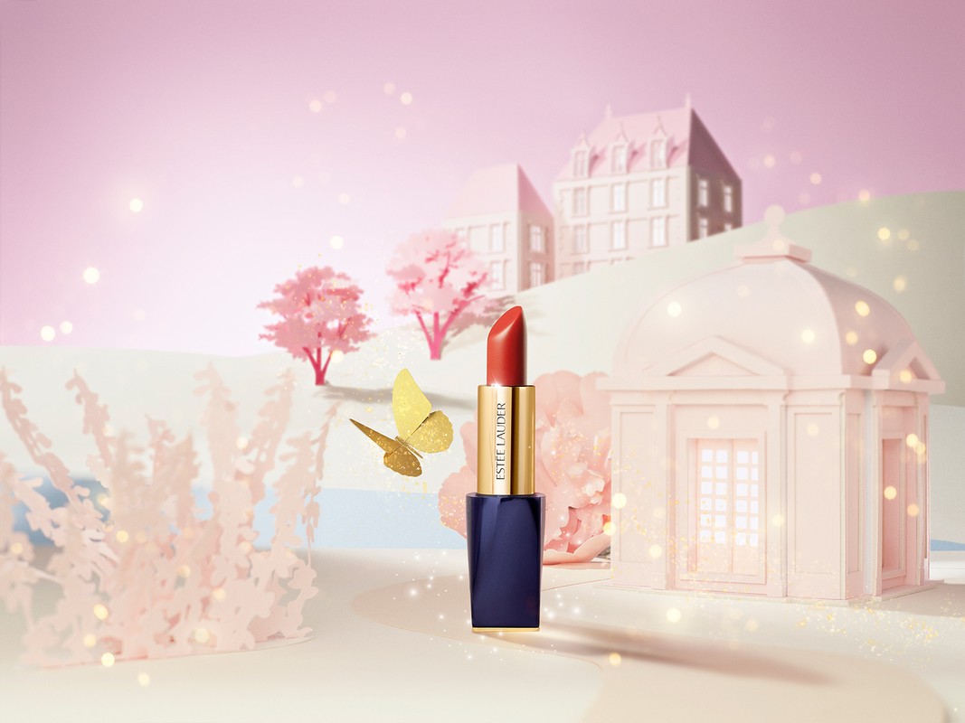 Red lipstick in a navy and gold tube displayed in a miniature pink set with buildings, cherry trees, and a golden butterfly.