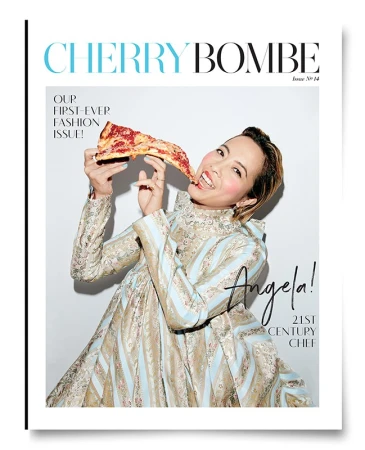 Woman in an ornate patterned dress eating a slice of pizza against a plain white background for Cherry Bombe magazine cover