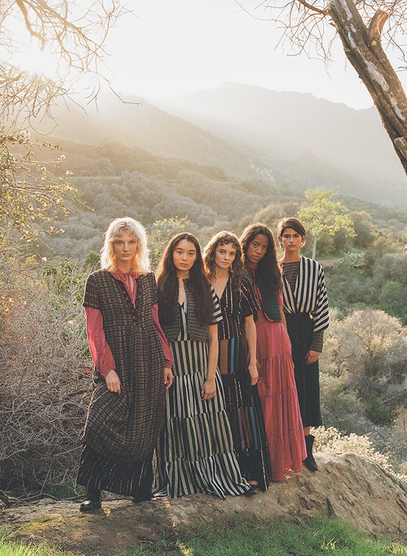 Five fashion models in dresses pose outdoors against a backdrop of mountains and trees in the sunlight, showcasing various striped fabrics.