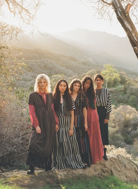 Five fashion models in dresses pose outdoors against a backdrop of mountains and trees in the sunlight, showcasing various striped fabrics.