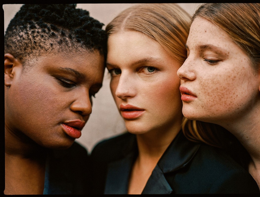 Three diverse women in a close-up studio shot featuring diverse skin tones and hairstyles, with soft lighting and a focus on skincare and beauty.