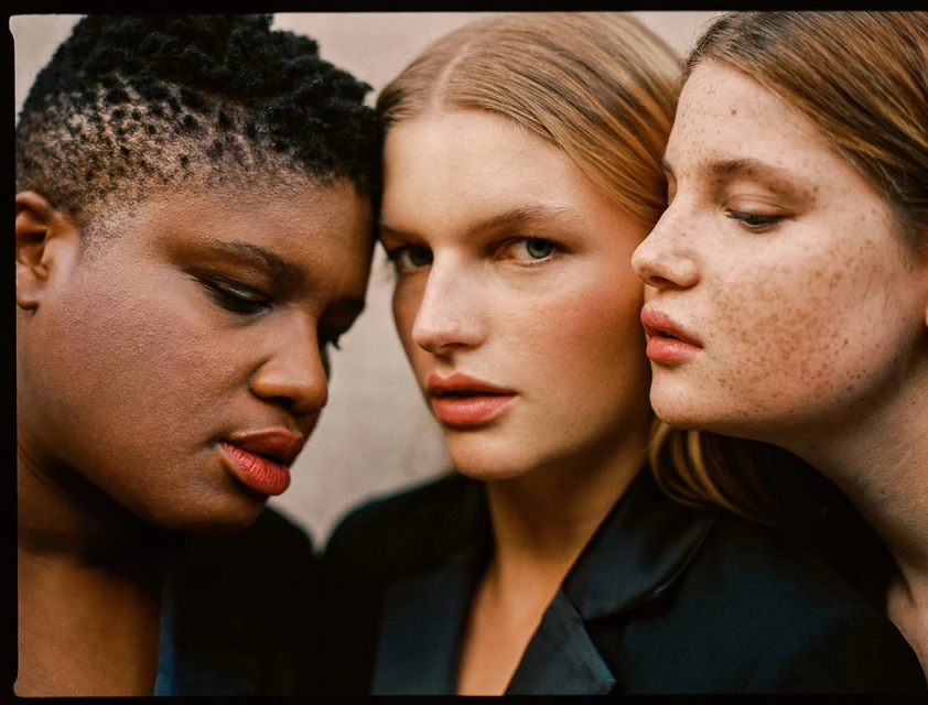 Three diverse women in a close-up studio shot featuring diverse skin tones and hairstyles, with soft lighting and a focus on skincare and beauty.