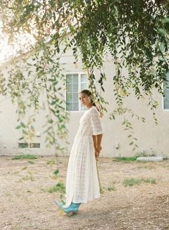 Woman in a white dress poses near a tree swing in a backyard setting with natural light, wearing turquoise boots for a fashion-forward look.