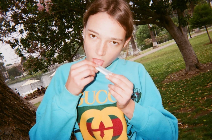 Young woman in a bright blue sweatshirt holding a rolling paper in a park setting.