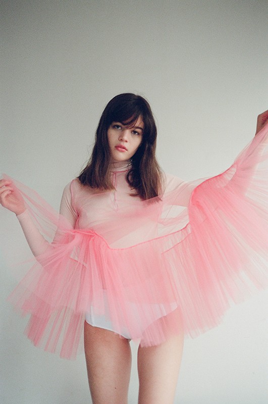 Young woman in pink tulle dress posing in front of a white wall in a studio setting, fashion photography.