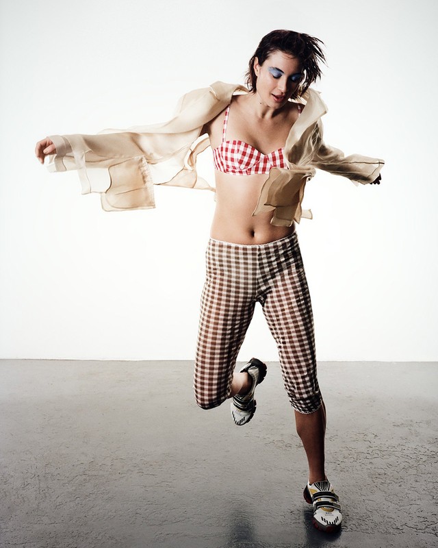 Woman in red and white gingham bra and leggings jumping against a bright studio background