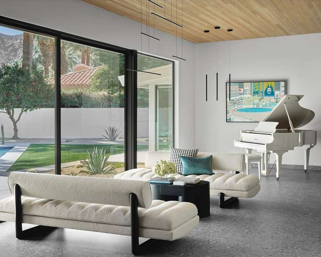 Living room with white couches, a black coffee table, a white grand piano, and a large window overlooking a backyard and swimming pool.