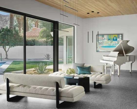Living room with white couches, a black coffee table, a white grand piano, and a large window overlooking a backyard and swimming pool.