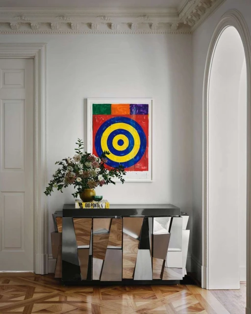 Interior design shot featuring a wooden cabinet with mirrored details, flowers in a vase, and colorful abstract art on the wall.