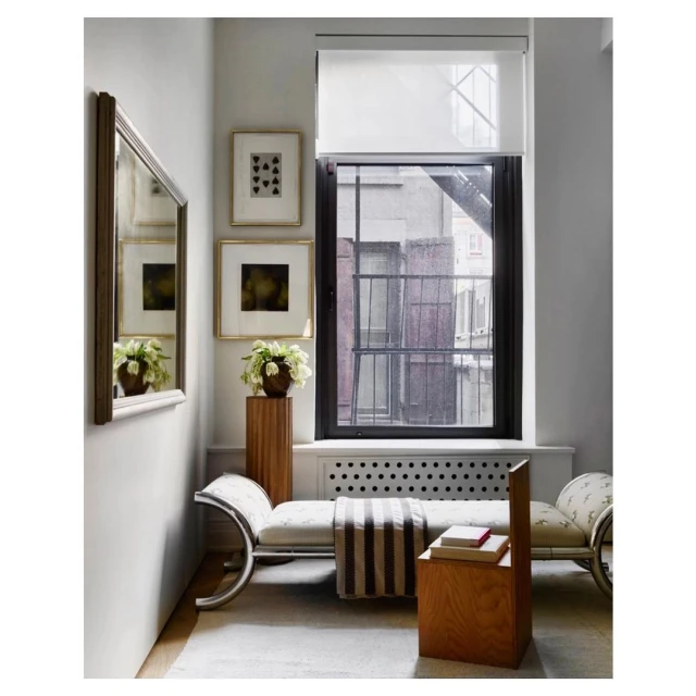 Interior view of a window seat nook with a white daybed, wooden accents, abstract art, and a view to a brick apartment building.