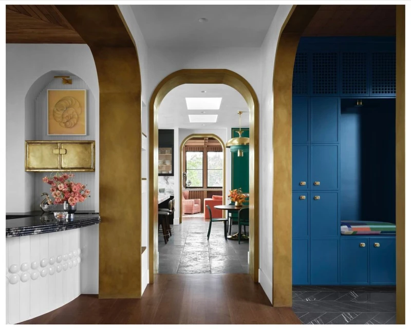 Interior view of a hallway featuring gold-trimmed arched doorways, leading to rooms with a dining set and seating area.