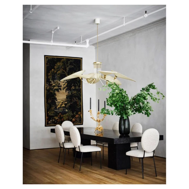 Formal dining room with a dark table surrounded by white chairs, featuring an ornate chandelier and tapestry against a light gray wall.
