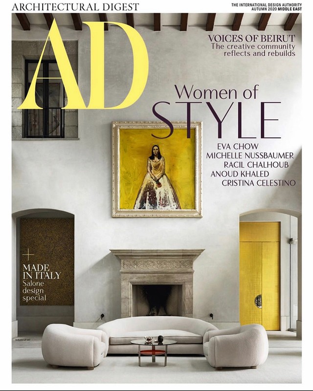 Architectural Digest cover featuring a living room interior with a painting, fireplace, sofa, armchairs, and a gold door.