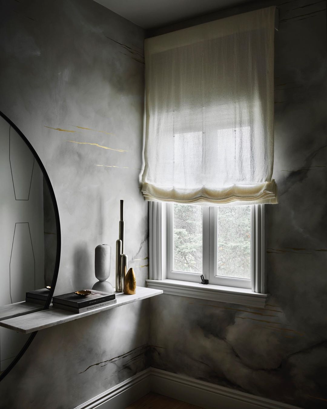 Interior corner featuring a floating marble shelf with decorative objects, a round mirror, a window with sheer blinds, and textured walls.