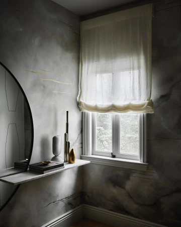 Interior corner featuring a floating marble shelf with decorative objects, a round mirror, a window with sheer blinds, and textured walls.