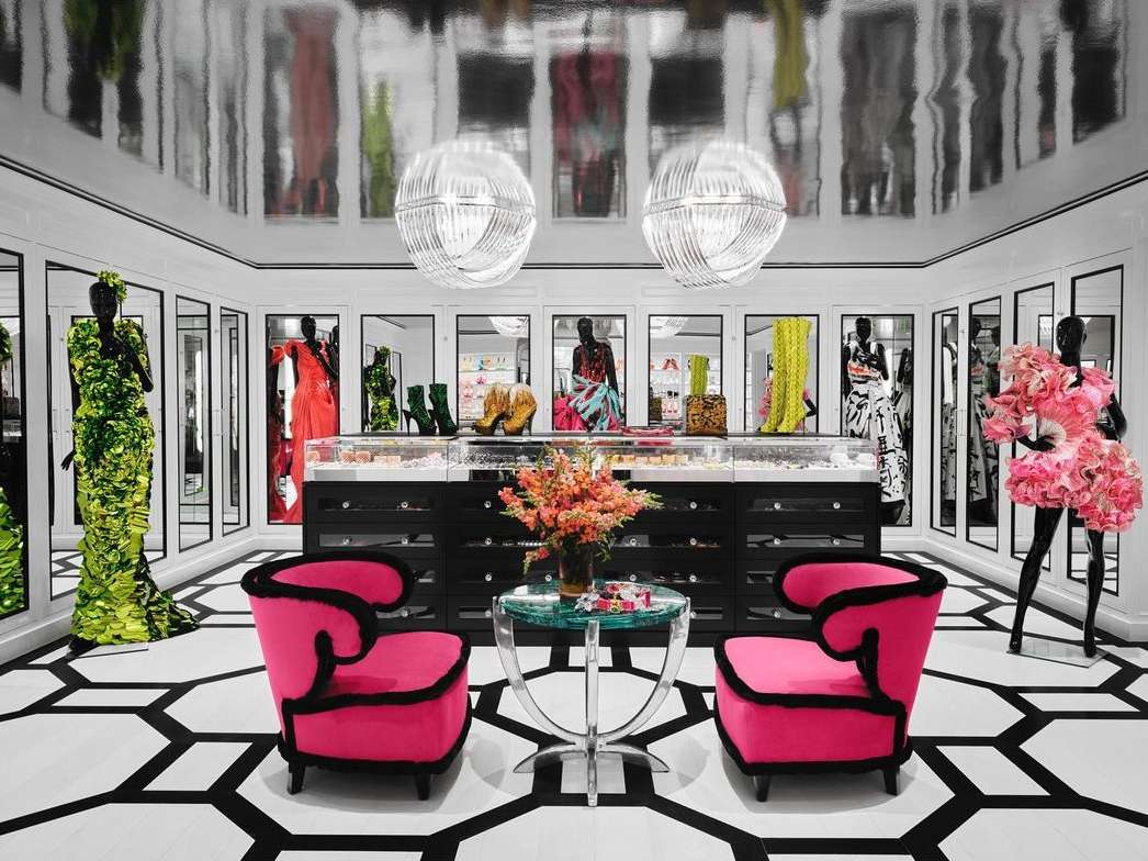 Fashion boutique interior featuring mannequins dressed in colorful couture gowns, set against black and white geometric flooring and mirrored displays.