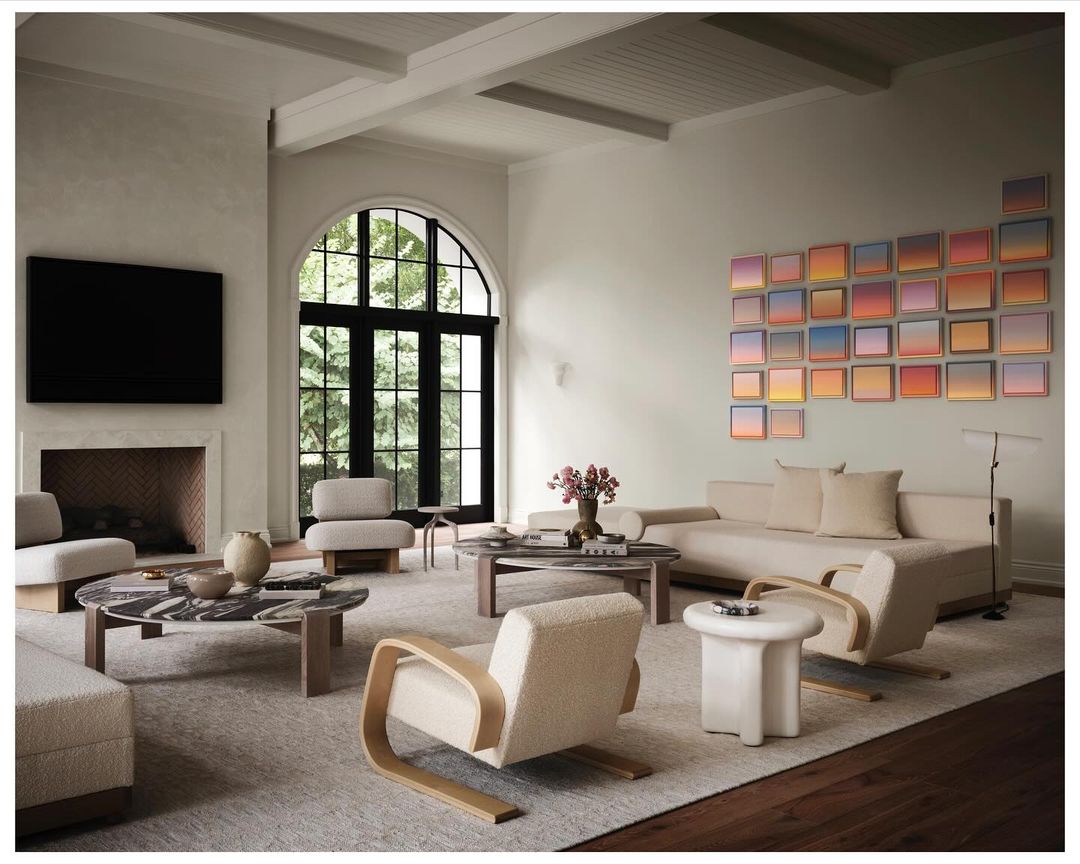 Living room interior featuring neutral-toned furniture, round coffee table, fireplace with mounted TV, and art in a bright, airy space.