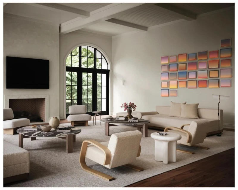 Living room interior featuring neutral-toned furniture, round coffee table, fireplace with mounted TV, and art in a bright, airy space.