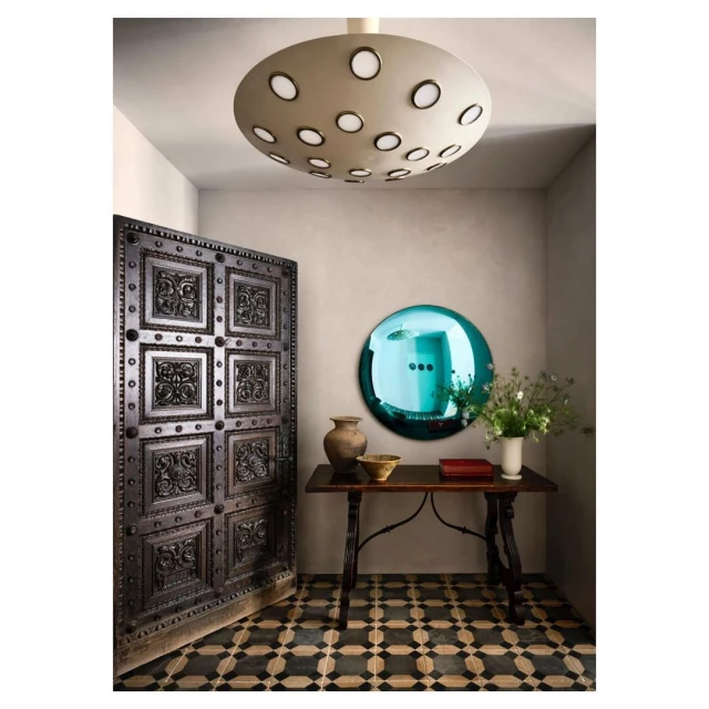 Interior entryway with an antique carved wooden door, a round blue mirror, decorative objects on a wooden table, and a patterned floor.