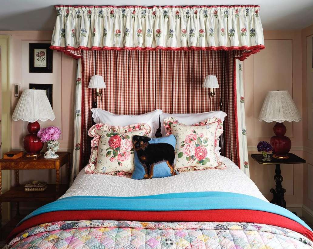 Charming bedroom interior with a four-poster bed featuring floral patterned pillows, a colorful patchwork quilt, and antique-style decor.