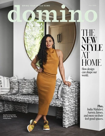 Magazine cover featuring Ayesha Curry in a mustard-colored dress and sneakers, leaning against a patterned bench with a round mirror behind.