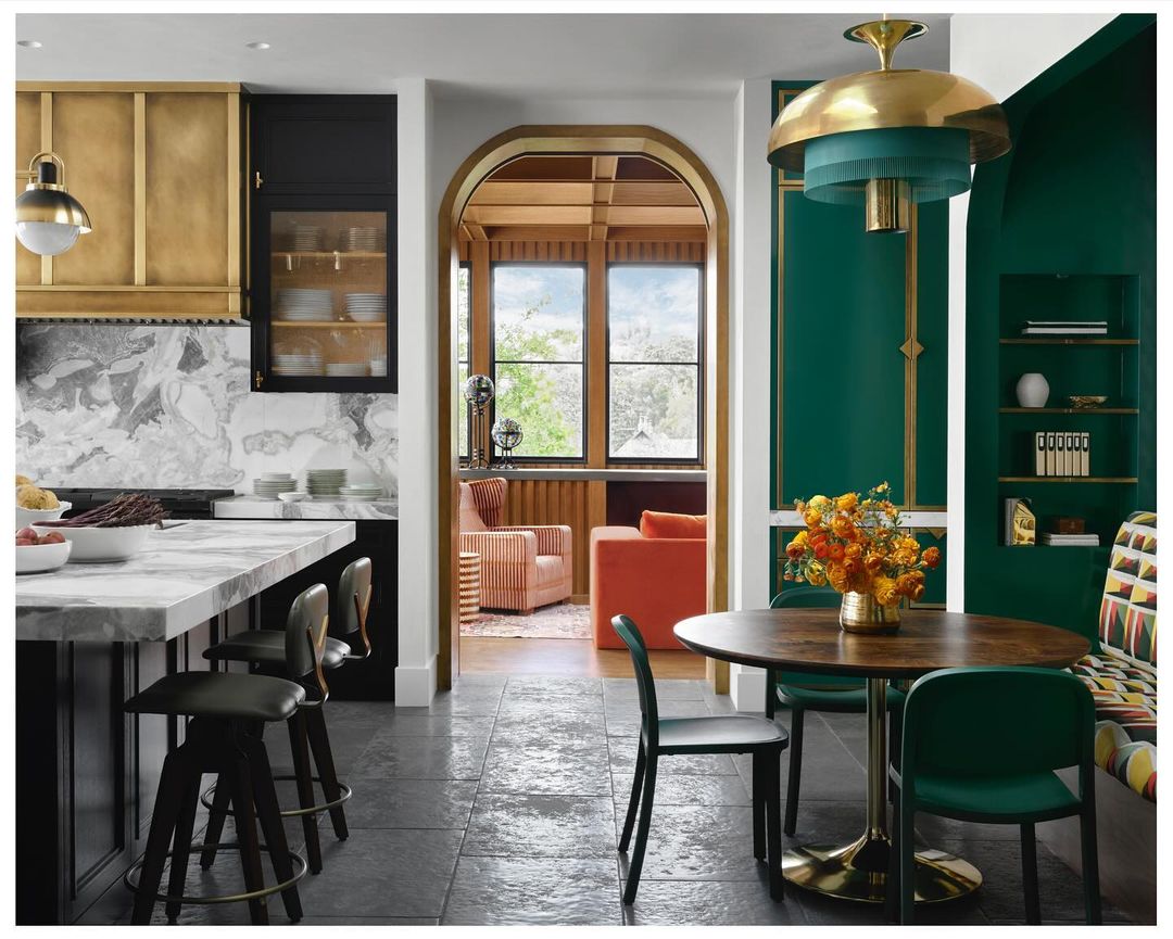 Interior view of kitchen and dining area showcases a modern kitchen with marble countertops, gold and black cabinets, dining set and orange lounge area.