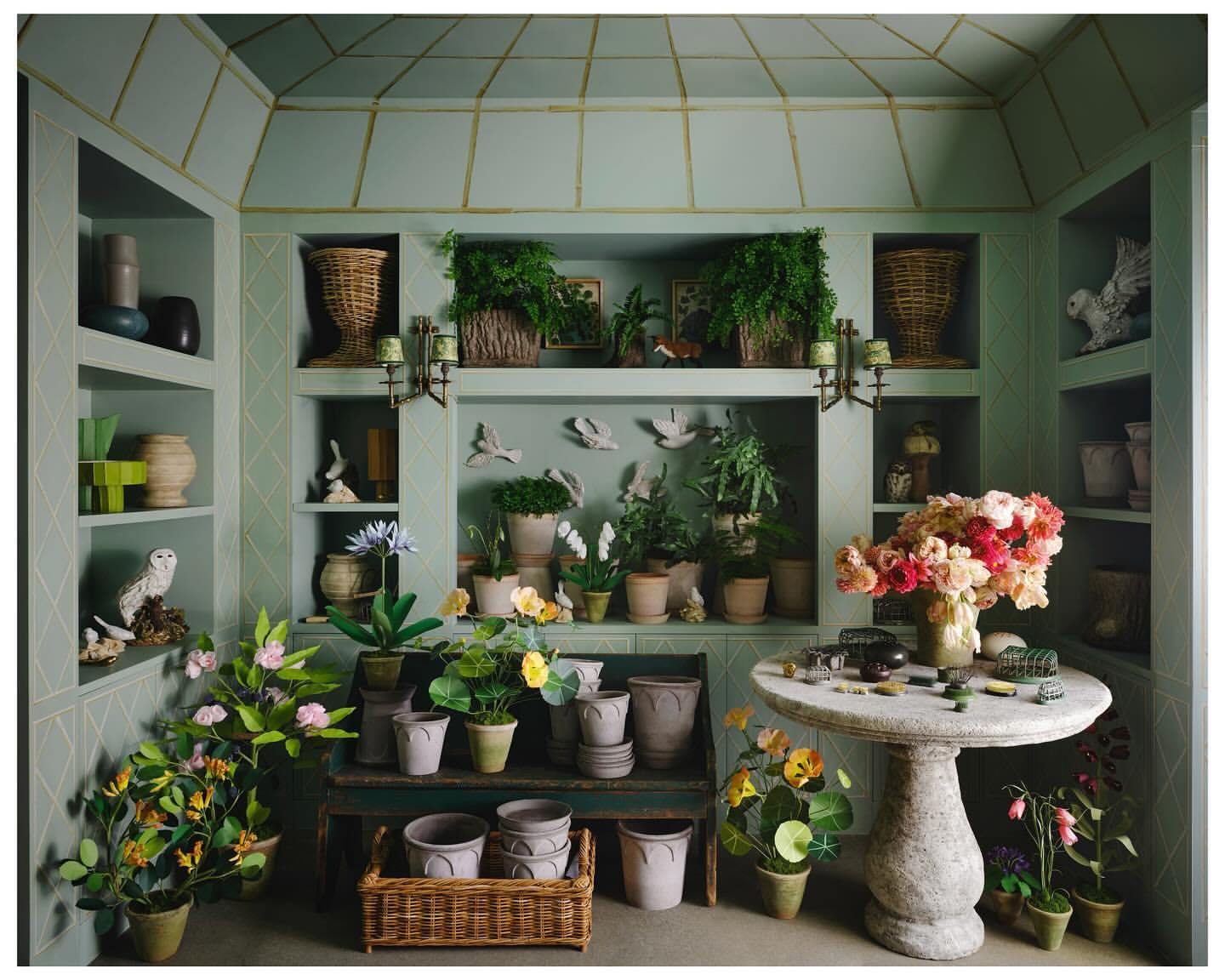 Indoor garden room featuring potted plants, flowers, and decorative objects displayed on shelves, tables, and window ledges.