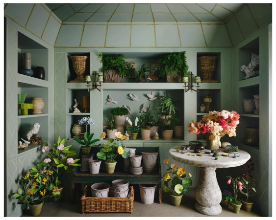 Indoor garden room featuring potted plants, flowers, and decorative objects displayed on shelves, tables, and window ledges.