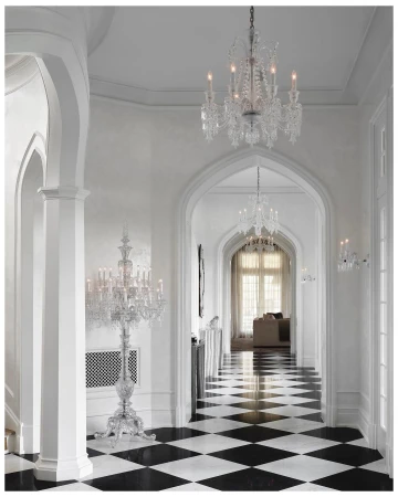 A bright, traditionally styled home foyer featuring black and white checkered tile flooring, white walls, archways, and ornate crystal chandeliers.