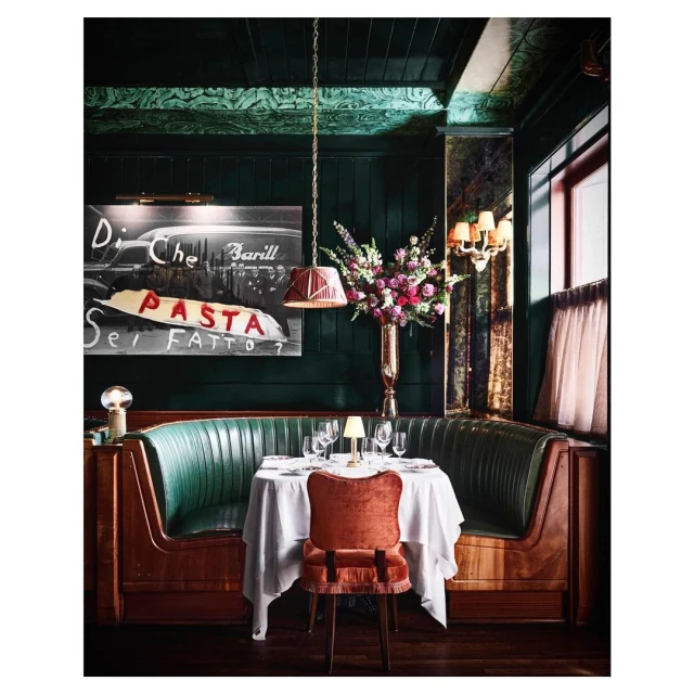 Interior of a restaurant with a booth, table set for dining, floral arrangement, and artwork with the word 'PASTA' visible.