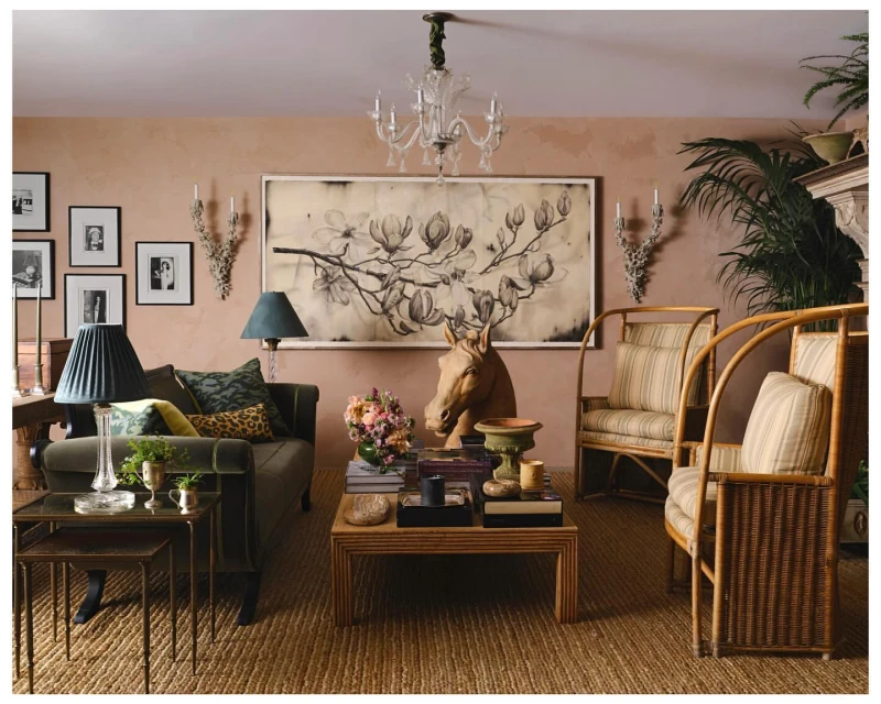 Living room interior with green sofa, rattan chairs, coffee table, botanical art, lamps, and plants in an eclectic style.