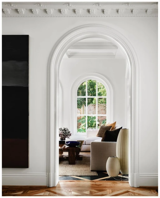 Living room interior with white walls, archway, wood floors, furniture, and natural light, showcasing a modern, bright, and airy home design.