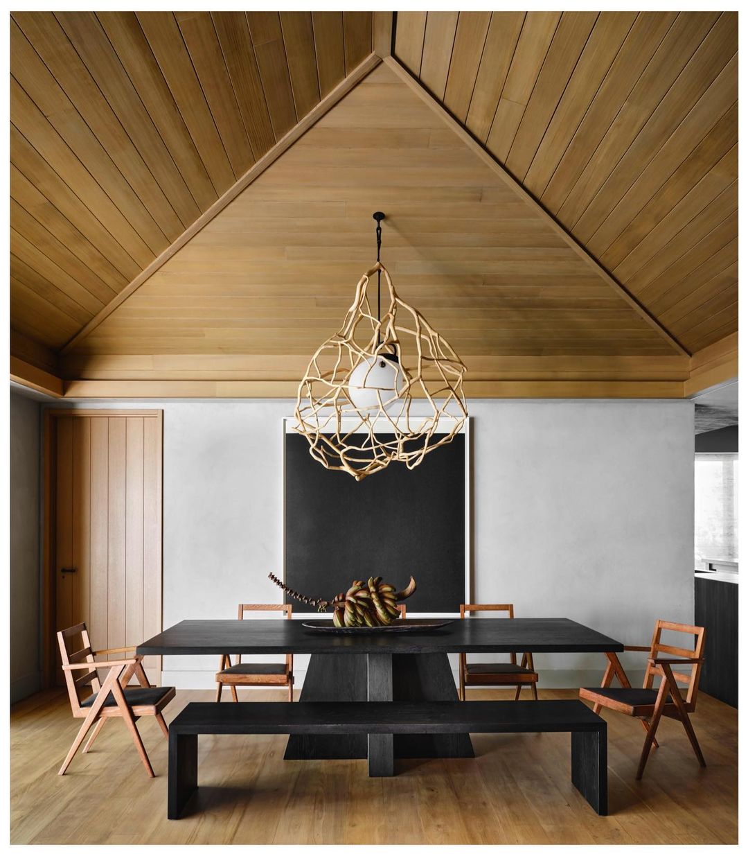 Contemporary dining room featuring a black table with sculptural decor, surrounded by wooden chairs, a bench, and an artistic light fixture.