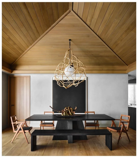Contemporary dining room featuring a black table with sculptural decor, surrounded by wooden chairs, a bench, and an artistic light fixture.