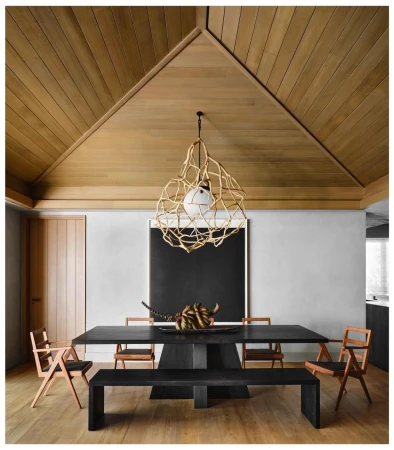 Contemporary dining room featuring a black table with sculptural decor, surrounded by wooden chairs, a bench, and an artistic light fixture.