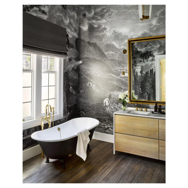 Interior of bathroom with freestanding tub, wood vanity, landscape wallpaper, framed mirror, and natural light from a window.