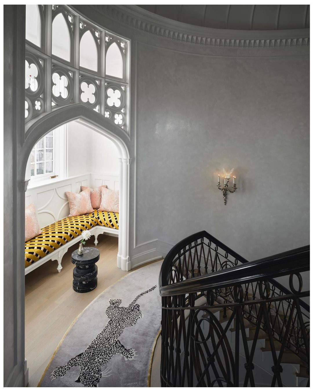Interior of a home with a staircase featuring wrought iron railings, a custom rug, and a window seat with pillows.