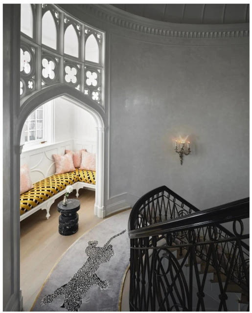 Interior of a home with a staircase featuring wrought iron railings, a custom rug, and a window seat with pillows.