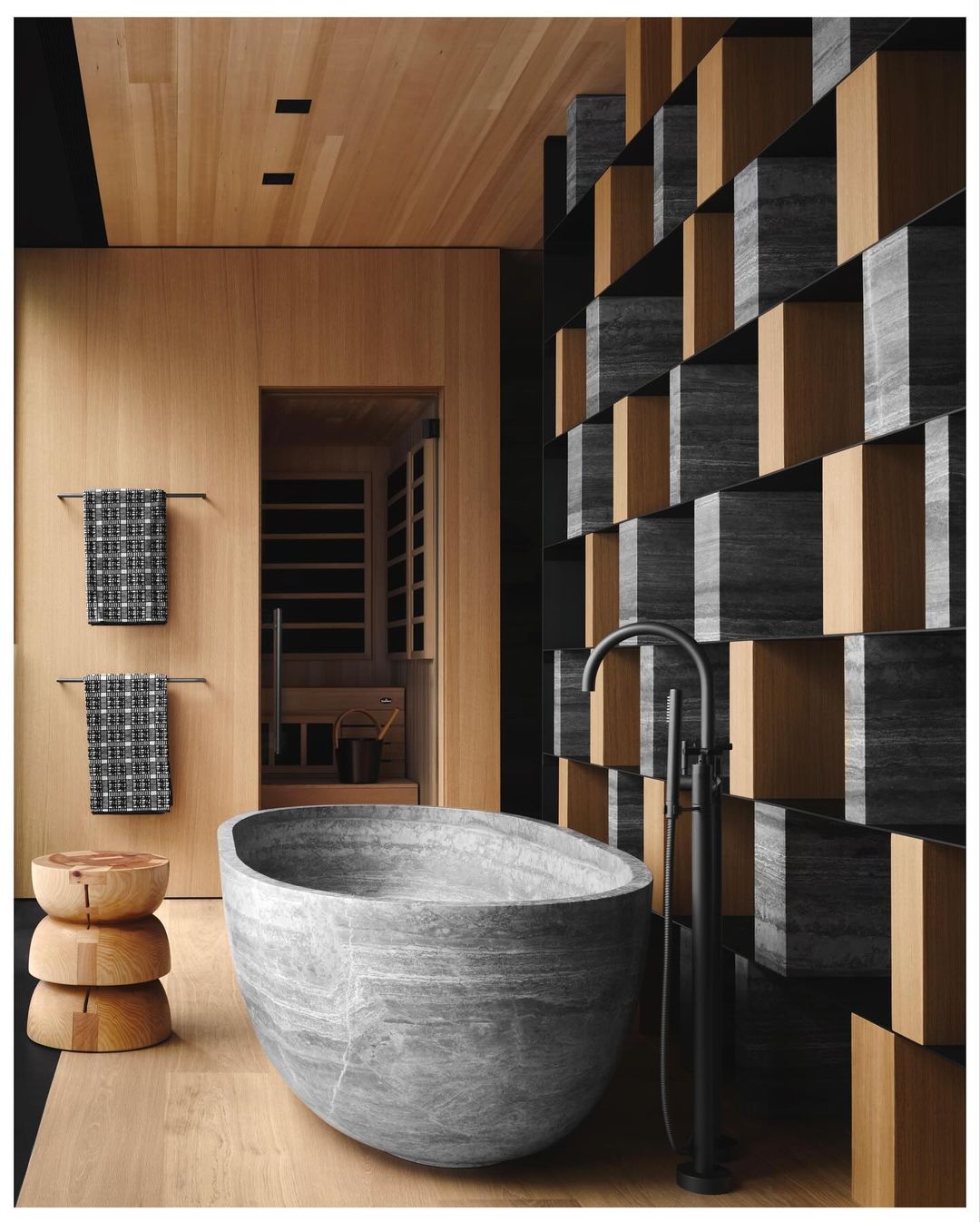 Stone bathtub is the focal point of a modern bathroom with wood paneled walls and floor, and a decorative partition.
