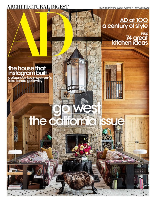 Architectural Digest magazine cover showcasing a rustic living room with stone fireplace, patterned sofas, and wood-paneled walls.