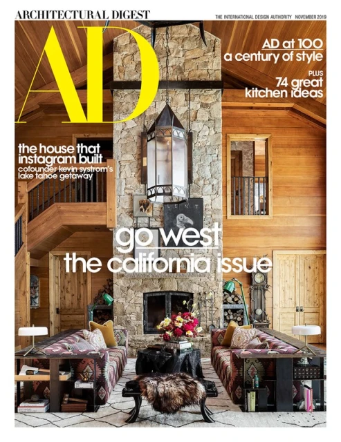 Architectural Digest magazine cover showcasing a rustic living room with stone fireplace, patterned sofas, and wood-paneled walls.