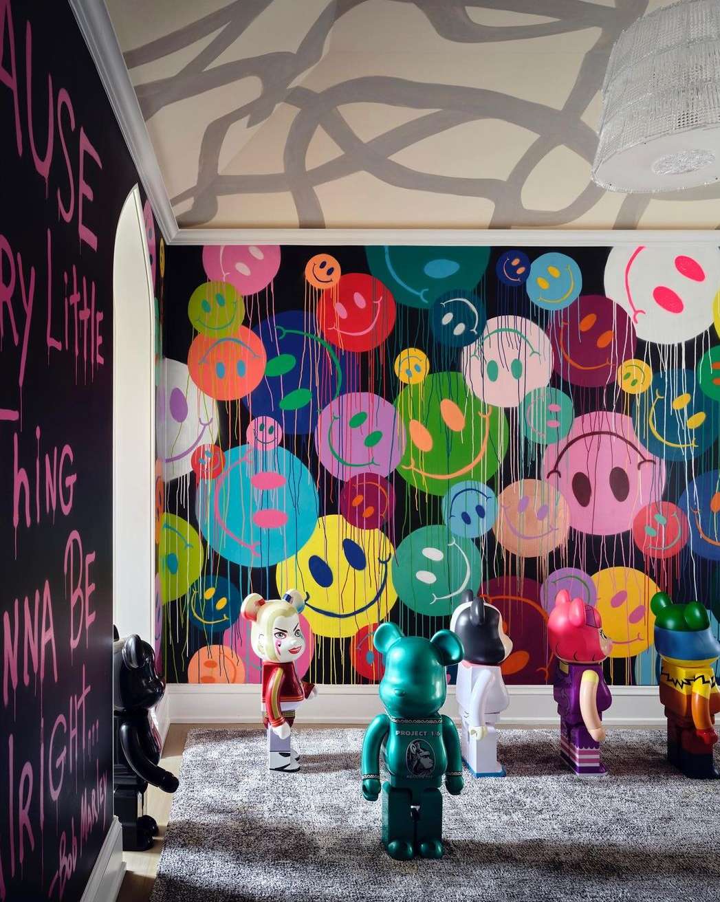 Colorful room with smiley-face art and designer toy figures. Black wall with text and a light-gray patterned ceiling.