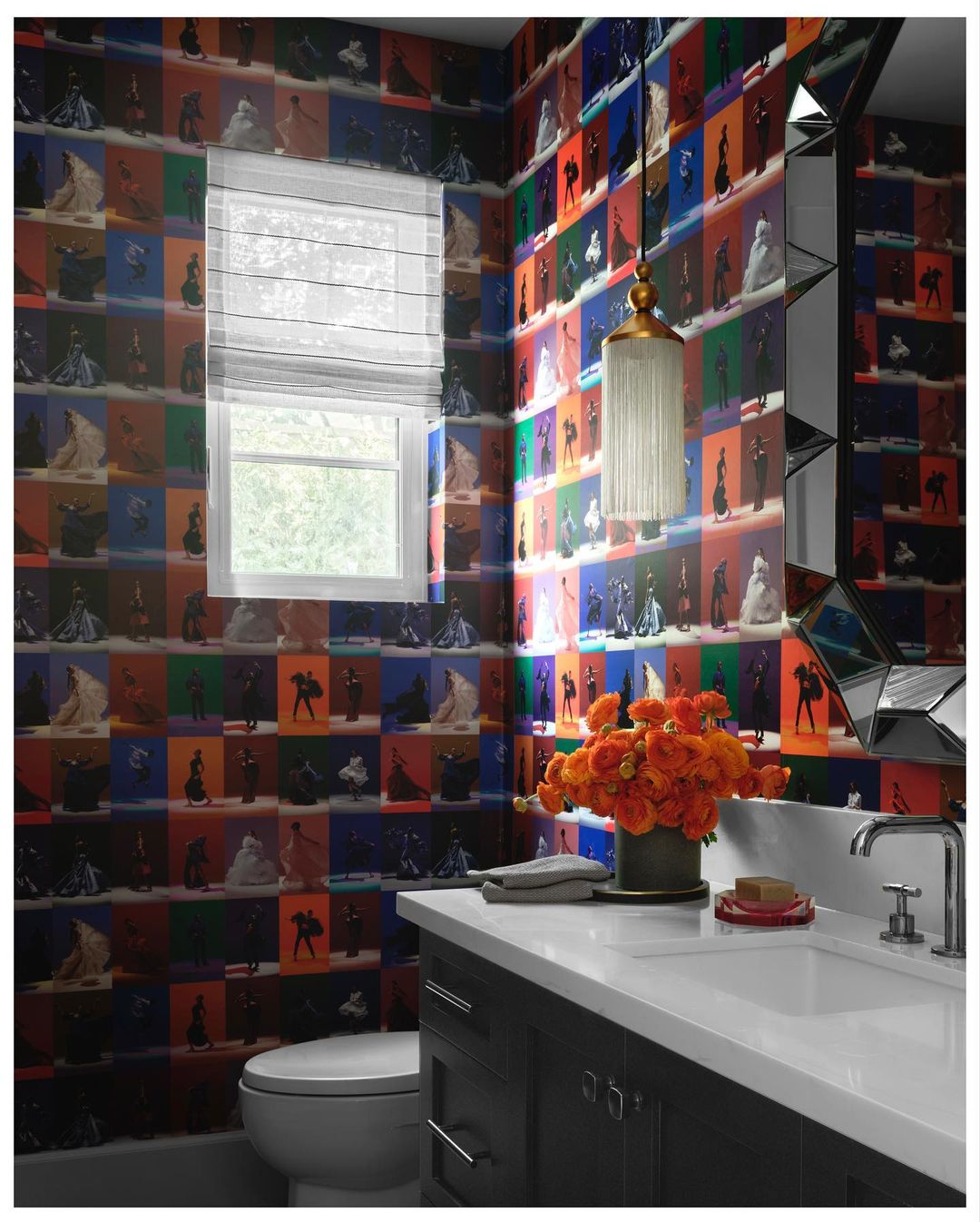 Powder room featuring bold wallpaper, a decorative mirror, sink and vanity, toilet, window, and orange flower arrangement.