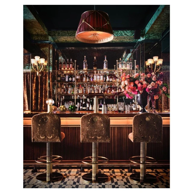 Elegant interior featuring a bar with three stools, a well-stocked liquor shelf, and a flower arrangement under a decorative lamp.