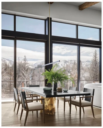 Modern dining room interior featuring a black table with green floral centerpiece, surrounded by six chairs and large windows showcasing a mountain view.