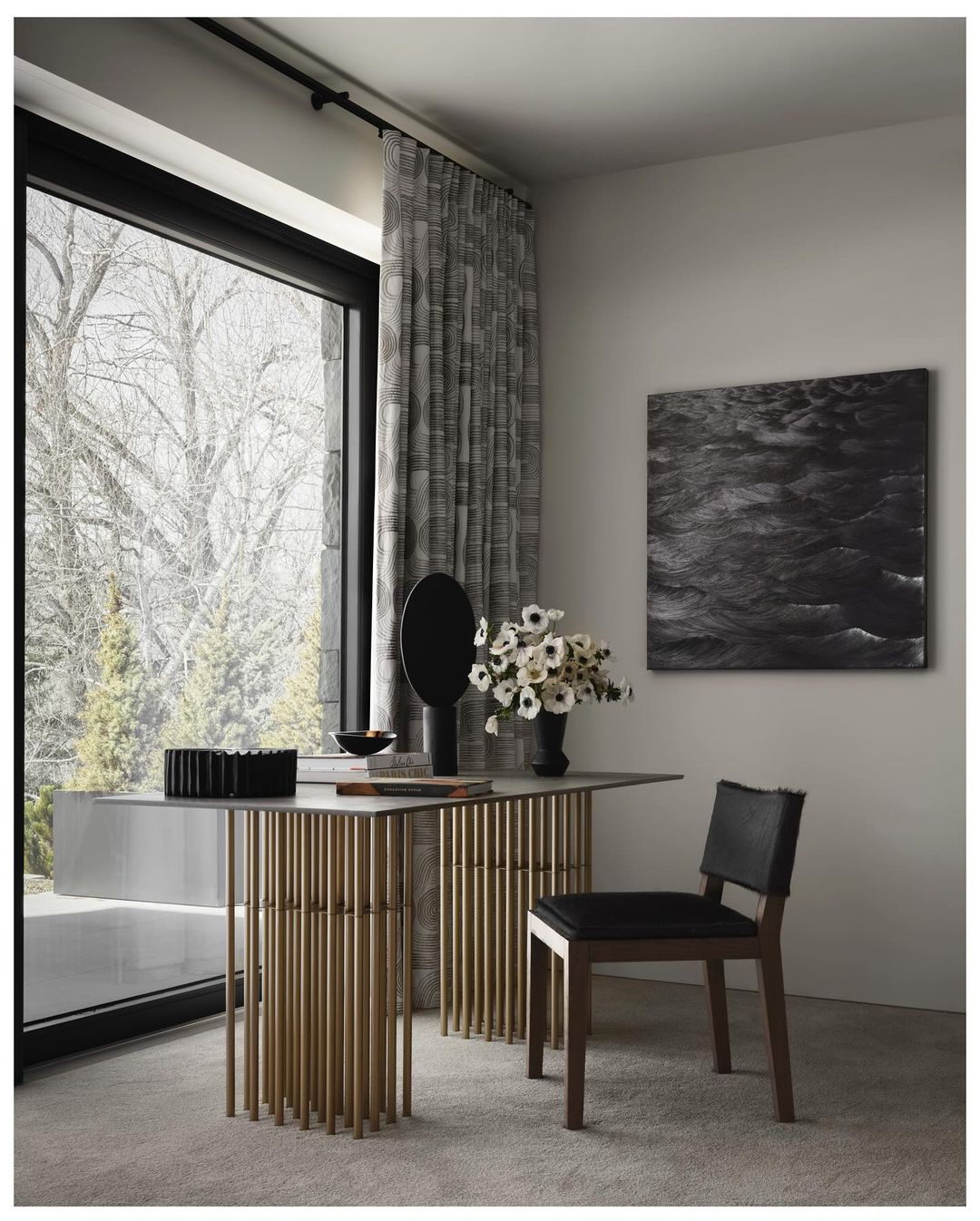 Contemporary interior with a console table featuring a gold tube base, complemented by a black vase with white flowers, and a chair.