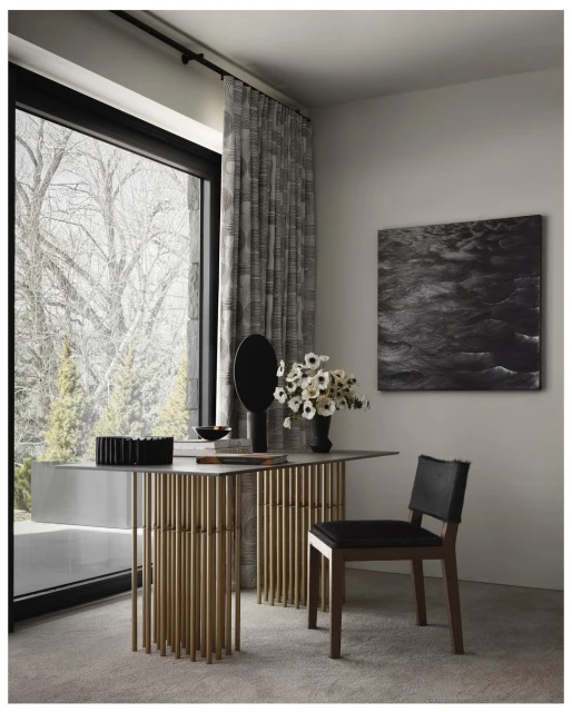 Contemporary interior with a console table featuring a gold tube base, complemented by a black vase with white flowers, and a chair.