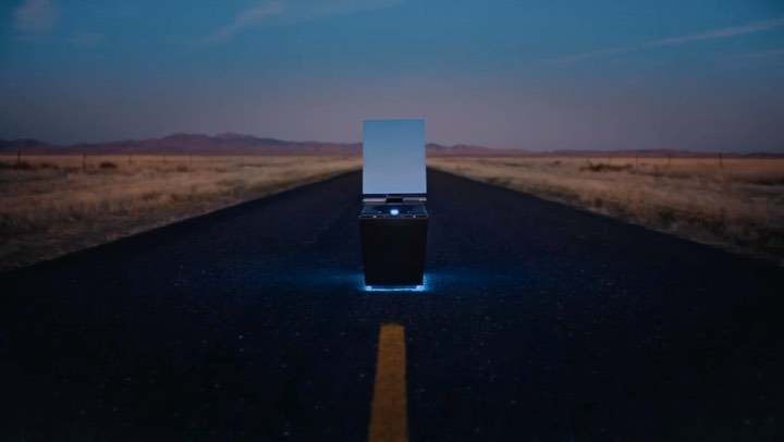 Modern dark object with reflective screen on highway at night. Desert landscape under twilight sky with blue accent lighting.