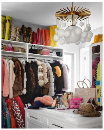 Well-organized walk-in closet featuring color-coordinated clothing, handbags, and shoes, illuminated by a modern bubble chandelier.